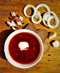 A delicious red borsch with sour cream, bread, onion, bacon and garlic on the wooden background