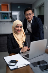 Fototapeta na wymiar asian malay couple working together at home with laptop and calculator