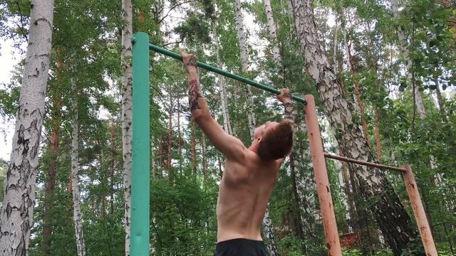 Young attractive man is doing exercise on the parallel bars outdoors. Guy shirtless is engaged in amateur sports. Active lifestyle concept.