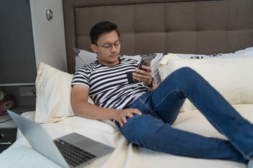 asian man using handphone and listening to music at bedroom