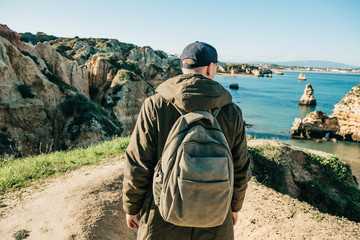 Fototapeta premium A tourist or traveler with a backpack admires the beautiful view of the Atlantic Ocean and the coast near the city called Lagos in Portugal.