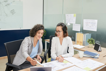Cheerful Vietnamese coworkers working on documents for presentation