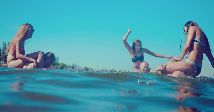 Group of happy friends of guys and girls splashing in the water on the beach