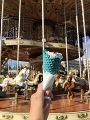 Woman's hand holding turquoise coloured ice cream cone against a merry-go-round in Moscow