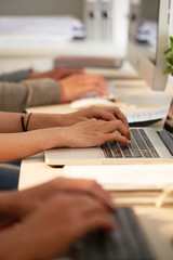 Hands of software developers working on computers at table in office