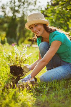 Young happy woman is planting a flower in her garden. 