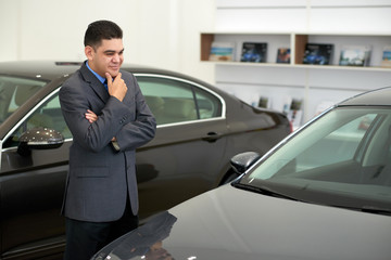 Smiling dreamy mixed-race man looking at car in showroom