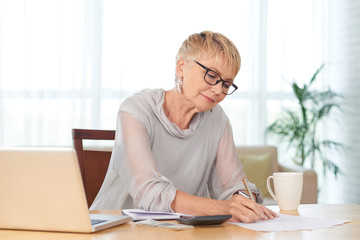 Elegant senior woman writing down household monthly expenses and
