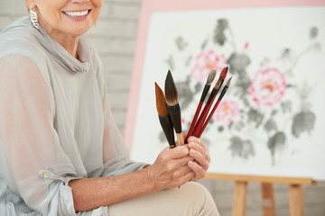 Set of various brushes in hands of elderly female painter