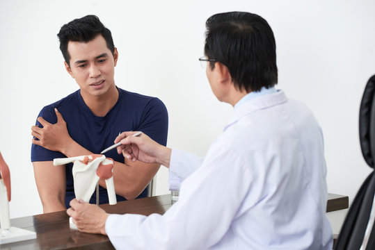 Doctor showing model of bone to patient who is suffering from pain in his shoulder