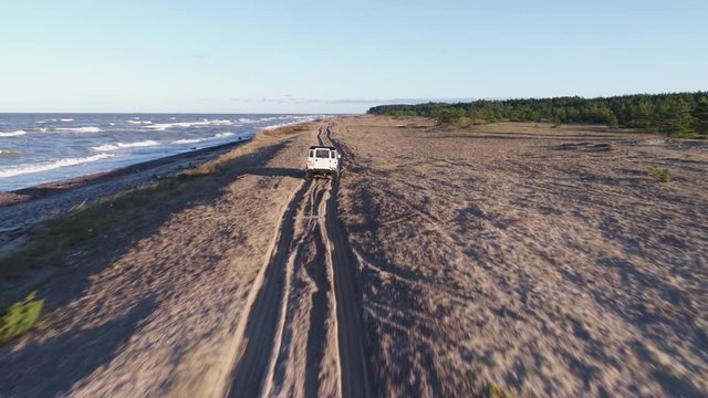 Aerial drone tracking shot of Land Rover Defender 90 driving on a sandy beach