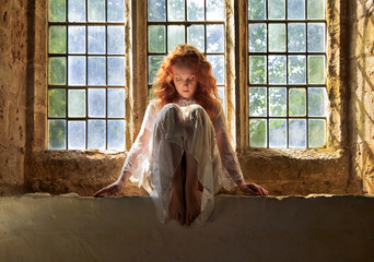Beautiful model with long red hair posing in a Gothic window