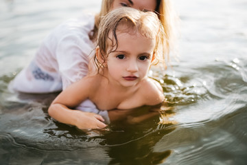 adorable daughter swimming together with mom in river and looking at camera