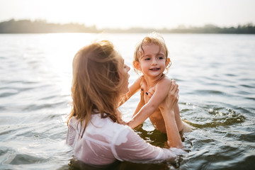 Fototapeta na wymiar mother holding happy daughter in river during sunset