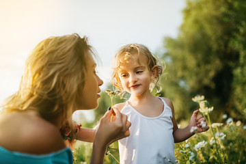 Obraz premium mother sniffing field flowers, smiling daughter looking at mom