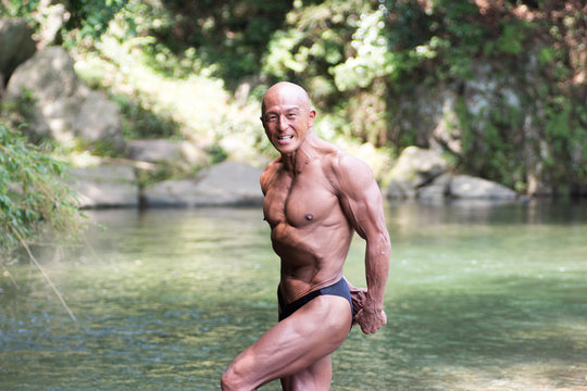 Japanese bald head bodybuilder posing the side triceps at the river