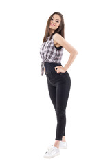 Fototapeta premium Side view of sexy young brunette lady in plaid shirt posing and smiling at camera. Full body isolated on white background. 