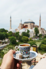 Naklejka premium Tradycyjny kubek kawy po turecku w ręku na tle meczetu Ayasofya.