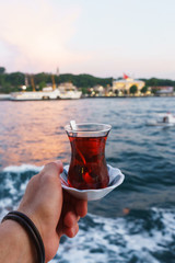Traditional black Turkish tea in a glass on a plate in the hands with a view of the Bosporus and Istanbul.