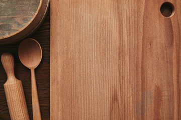 top view of wooden cutting board, spoon, rolling pin and sieve on table