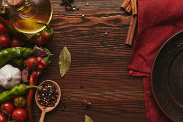 top view of red tablecloth, round plate, spices and vegetables on wooden surface