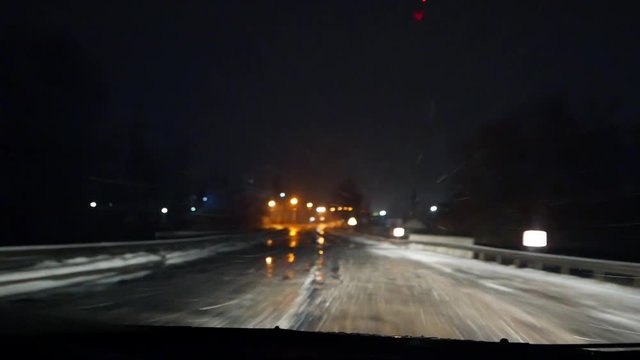 Night driving in the car in the snowfall on the wet snow road. Low beam and high beam of headlighs. Road safety