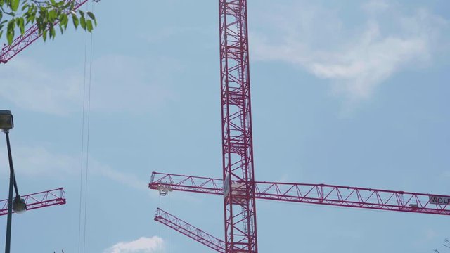Red cranes moving on city construction site against blue sky.