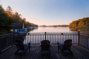 Naklejka premium Trio of Muskoka chairs on a patio overlooking Lake Joseph at dawn.