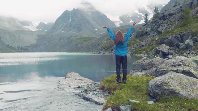 Altai, Kucherla, RUSSIA: Girl against a blue lake and mountains. The girl is spinning. Hands up. 4k Slow motion