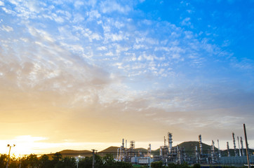 Oil refinery and sunset sky have mountain in background this sky is beautiful orange color and blue color  the refinery have a lot of chimney ,this image in energy and oil refinery concept