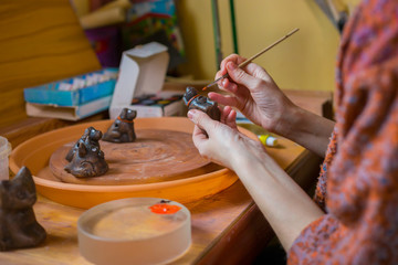 Fototapeta na wymiar Professional woman potter, decorator painting ceramic souvenir penny whistle toy dog in pottery workshop, studio. Crafting, artwork and handmade concept