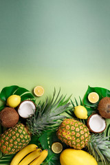 Exotic pineapples, coconuts, banana, melon, lemon, tropical palm and monstera leaves on green, turquoise background with copyspace. Creative layout. Monochrome summer concept. Flat lay, top view.