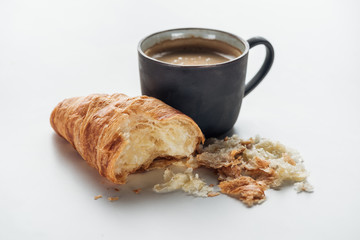 close-up shot of coffee cup and bitten croissant on white