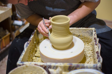 Professional male potter shaping jug with special tool in pottery workshop, studio. Crafting, artwork and handmade concept