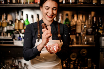 Happy smiling barman girl crushing a piece of ice for making a cocktail