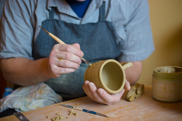 Fototapeta na wymiar Professional potter making pattern on clay mug with special tool in pottery workshop, studio. Crafting, artwork and handmade concept