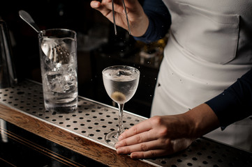 Barmaid hand putting an olive into a cocktail glass