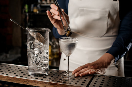 Bartender putting an olive into a cocktail glass