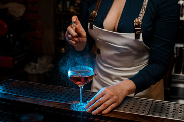 Sexy woman barman spraying blue-colored bitter on the glass