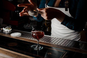 Barman decorating a strong and sweet summer cocktail sugar powder with orange and cherry