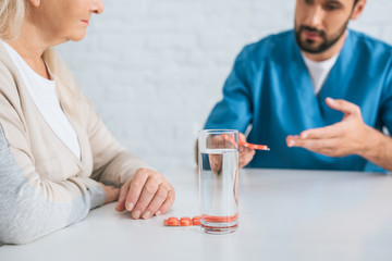 cropped shot of male nurse giving pills to senior woman