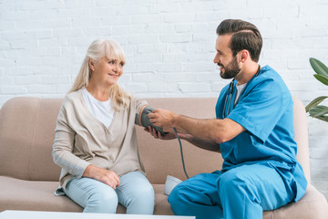 smiling male nurse measuring blood pressure to senior woman