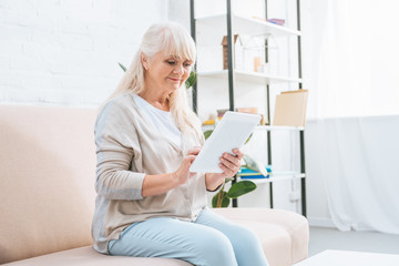 smiling senior woman using digital tablet while sitting on couch