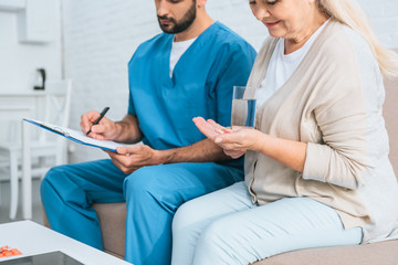 cropped shot of senior woman taking medicine and male nurse writing on clipboard