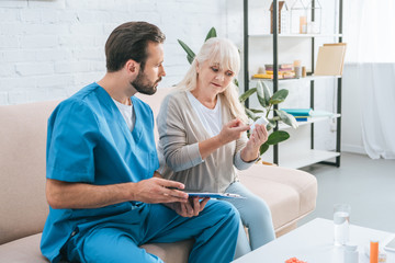 Obraz premium male nurse with clipboard looking at senior woman holding pills