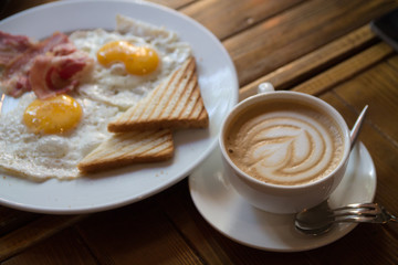 breakfast with fried eggs, bacon, toasts and cappuccino