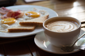 breakfast with fried eggs, bacon, toasts and cappuccino