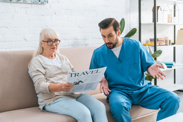 shocked male nurse looking at senior woman in eyeglasses reading travel newspaper