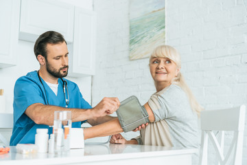 Obraz premium male nurse measuring blood pressure to smiling senior woman