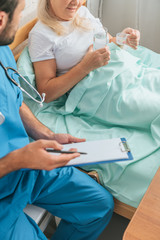 Obraz premium cropped shot of doctor writing on clipboard while senior woman taking medicine in bed